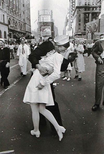 14 августа 1945 новость о капитуляции Японии возвестила окончание Второй мировой войны. Бурное празднование началось и на улицах Нью-Йорка, но, возможно, ни один из жителей города не чувствовал себя в тот момент более свободным, чем военные. Среди счастливых людей, собравшихся в тот день на Таймс-сквер, был и один из самых талантливых фотокорреспондентов 20-ого столетия, немецкий иммигрант по имени Альфред Эйзенштадт. Выхватывая своей камерой картины празднования, он приметил моряка, "идущего по улице и хватавшего каждую девочку в поле своего зрения." Позже моряк объяснил, что ему было наплевать, была ли она "бабушкой, крепкой, худой, старой или молодой" - он не делал никаких различий...